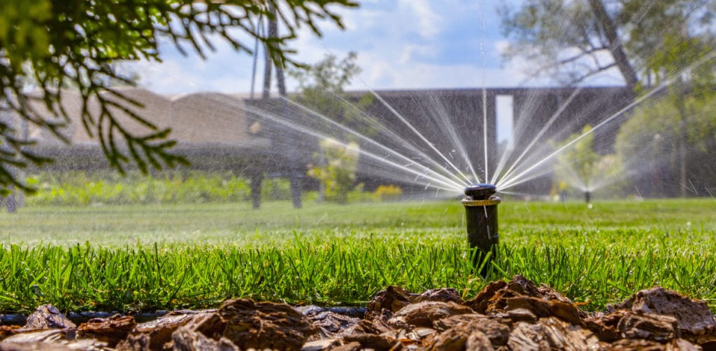 A sprinkler watering a green, lush lawn cared for by Scott's lawn Care property maintenance services.