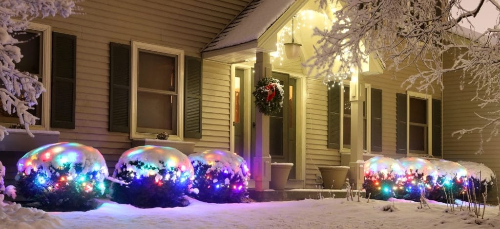 Home decorated for Christmas with snow-covered shrubs with lights