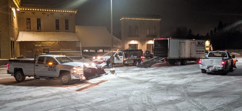 The Scott's Lawn Care truck and snowplow fleet in the winter at night in front of the General Store of Minnetonka
