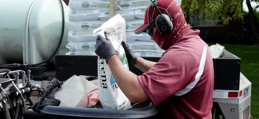 A Scott's Lawn Care professional dumps a bag of fertilizer into a machine.