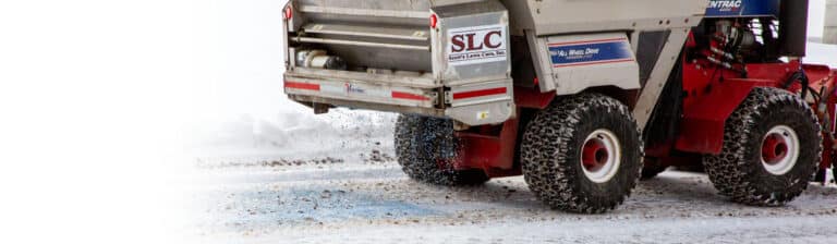An image of a Scott's Lawn Care ice removal vehicle evenly distributing salt on the street below to melt the ice during a cold Minnesotan winter.